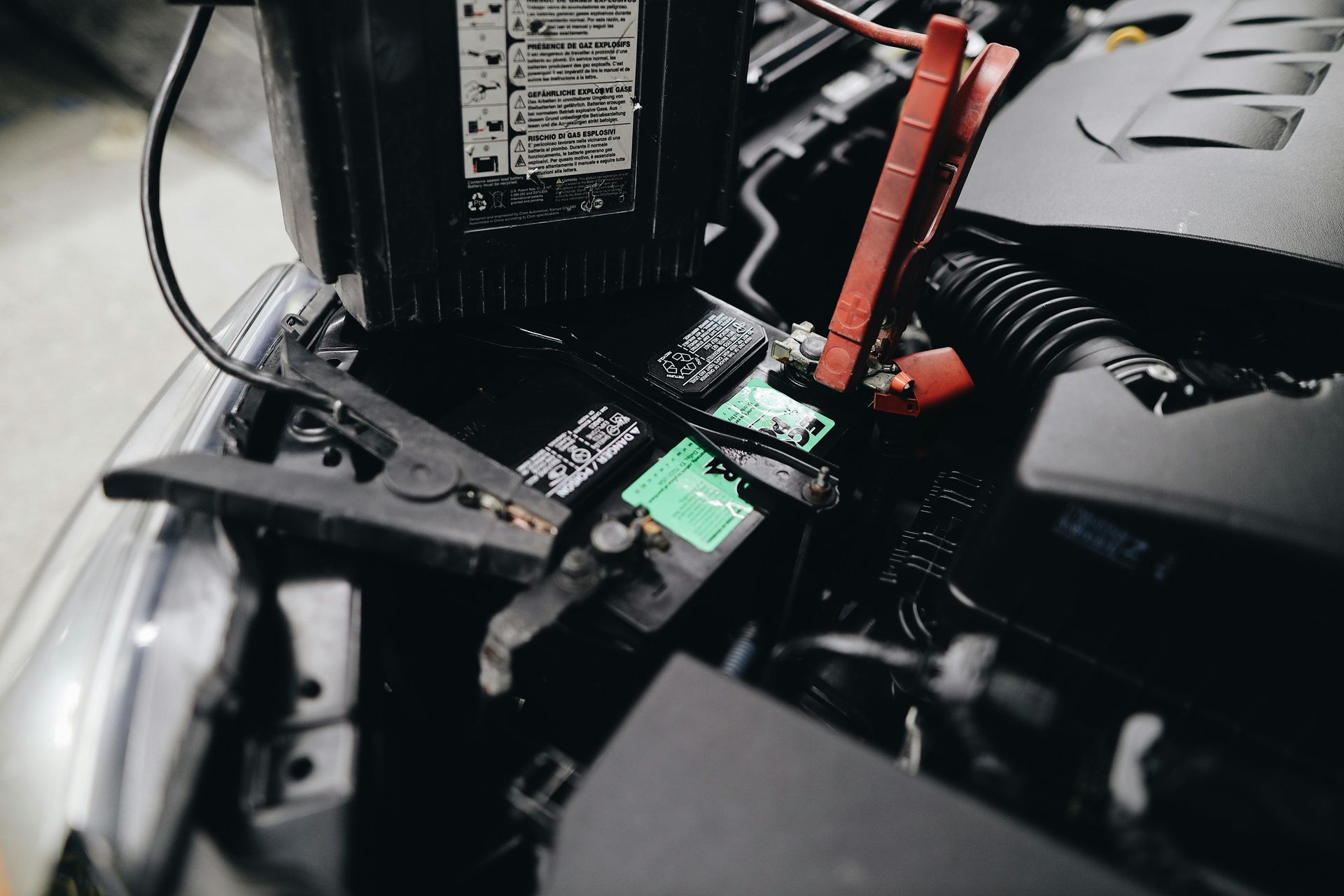 Detailed view of a car battery being jump-started with cables in an engine bay.